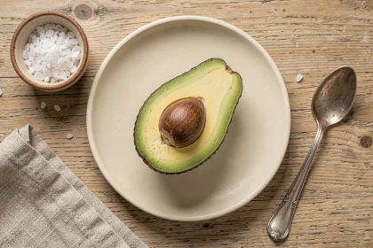 Moitié d'avocat mûr sur une assiette en céramique crème avec sel de mer et cuillère vintage, vue de dessus